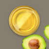 Glass dish of avocado oil with a sliced avocado on a gray background