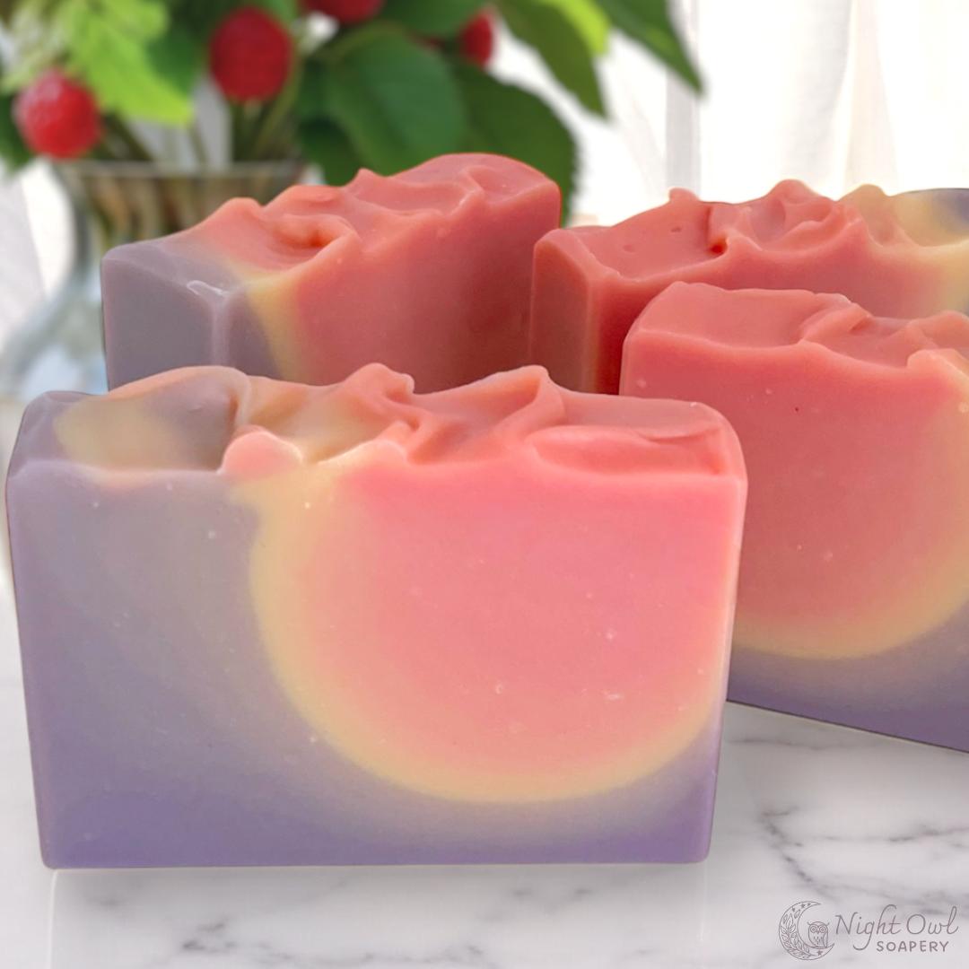 Gradient pink and purple soap bars on a marble surface with a blurred plant in the background.