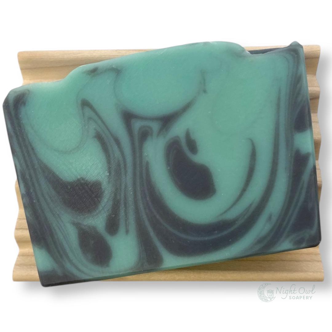 Marbled teal and black soap bar on a wooden dish
