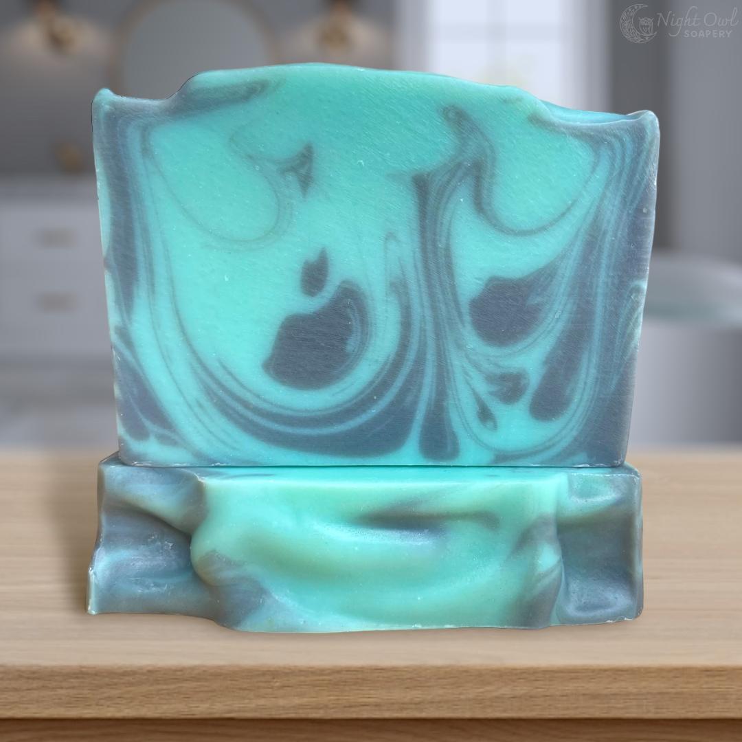 Two marbled teal and black soap bars stacked on a wooden surface