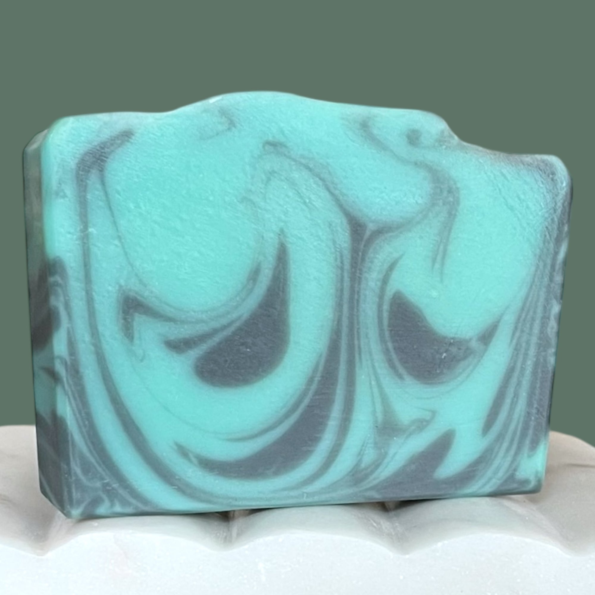 Swirled turquoise and black soap bar on a white surface with a green background