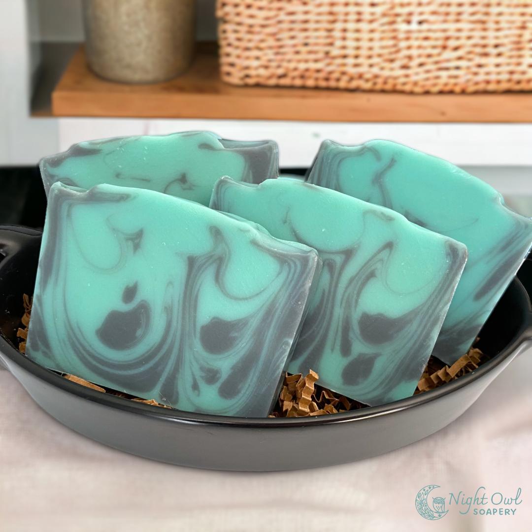 Teal and black marbled soap bars in a black dish on a wooden surface.