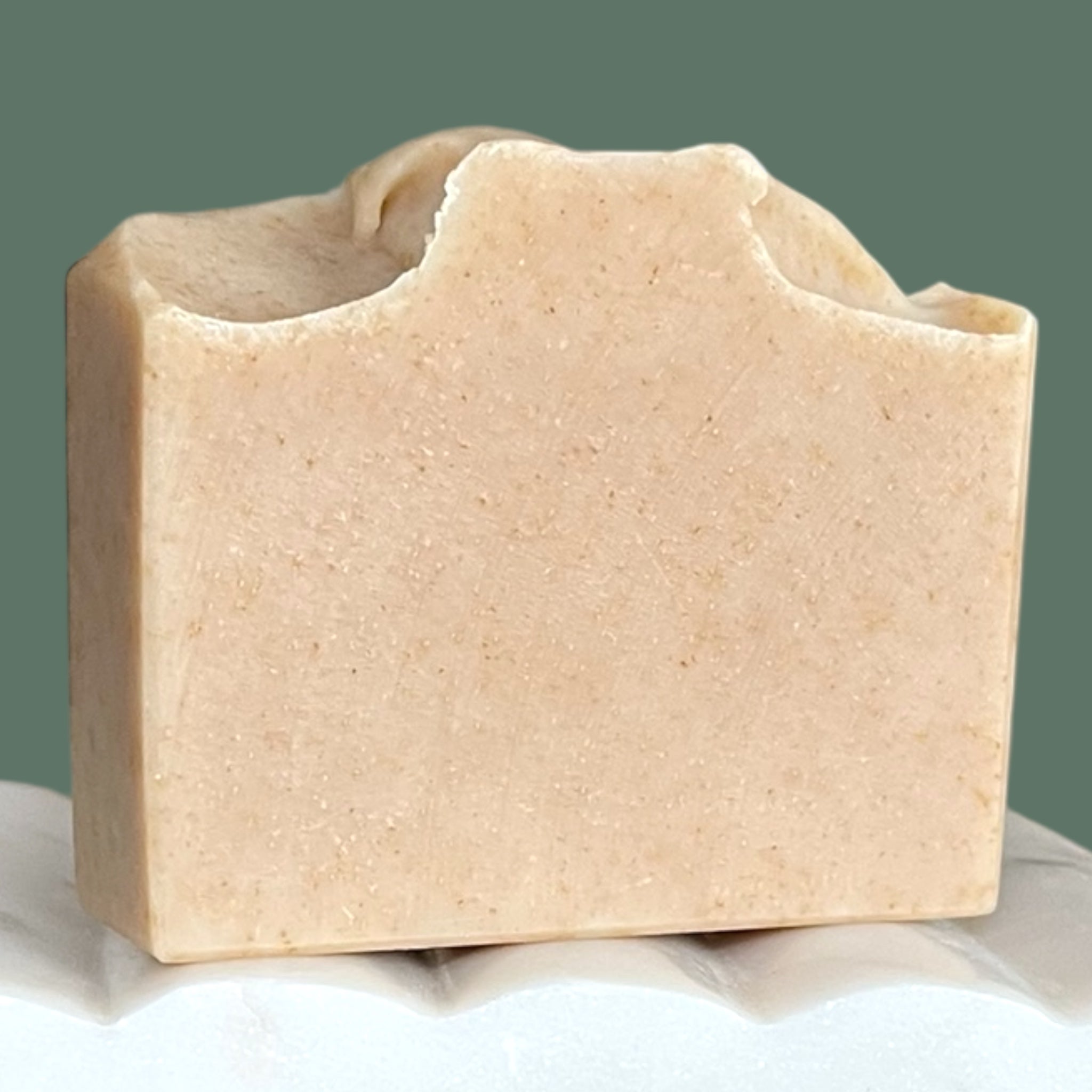 Bar of beige soap on a white surface with a green background