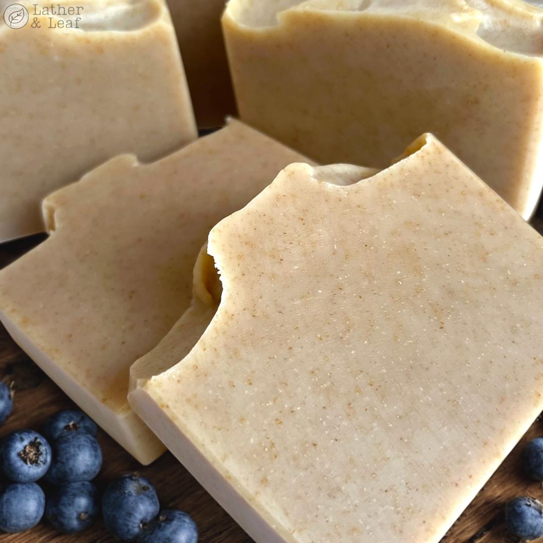 Close-up of soap bars with blueberries on a wooden surface, featuring the brand 'Lather & Leaf'.