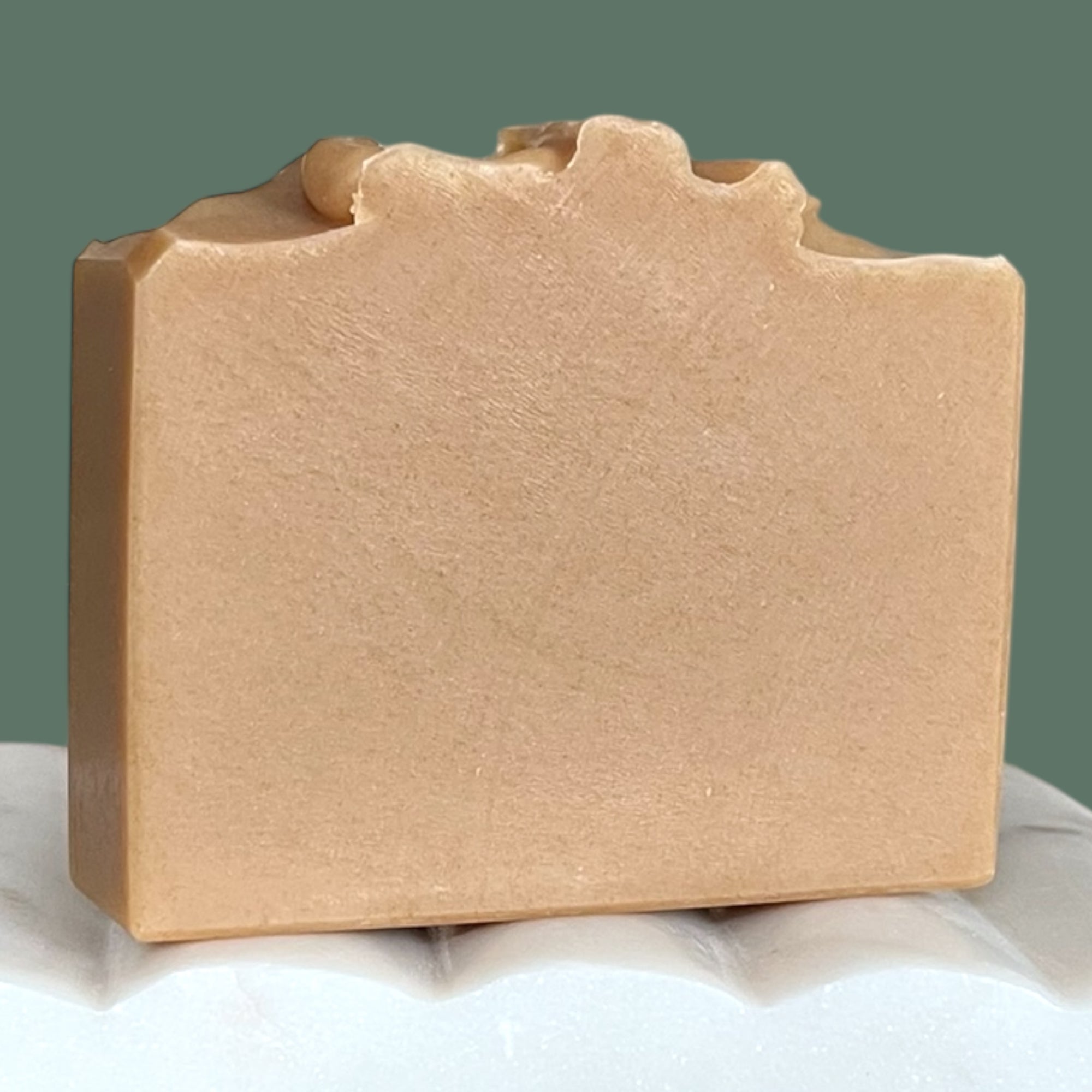 Bar of brown soap on a white surface with a green background