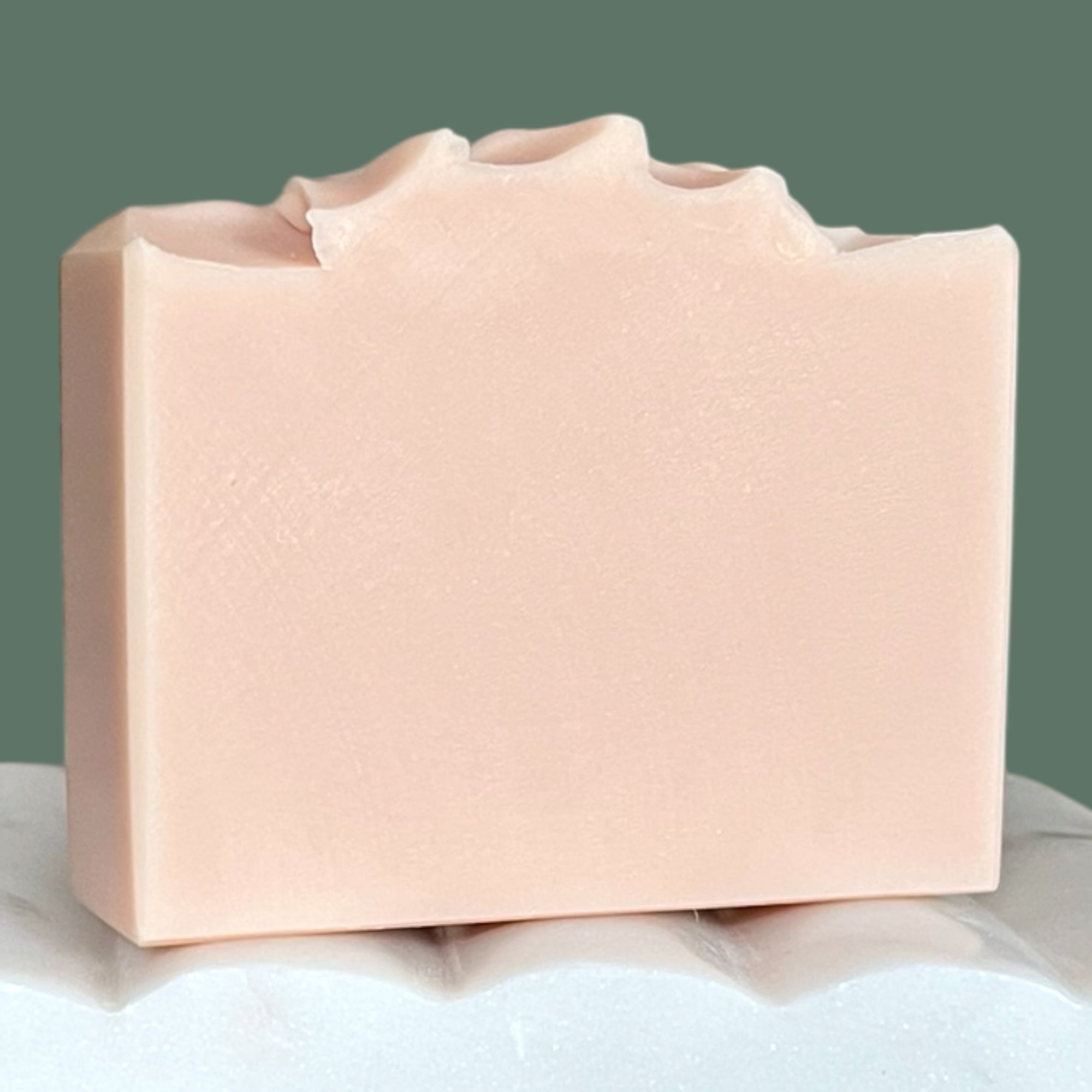 Light pink bar of soap on a white surface with a green background