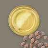 Glass container of oil with castor beans on a brown background