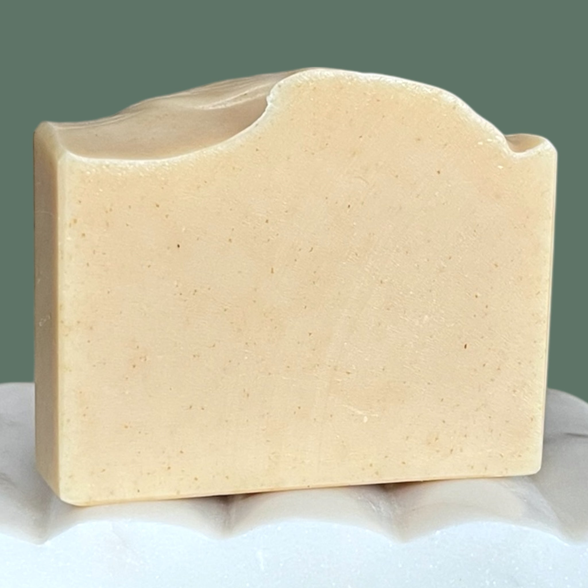 Beige bar of soap on a white surface with a green background