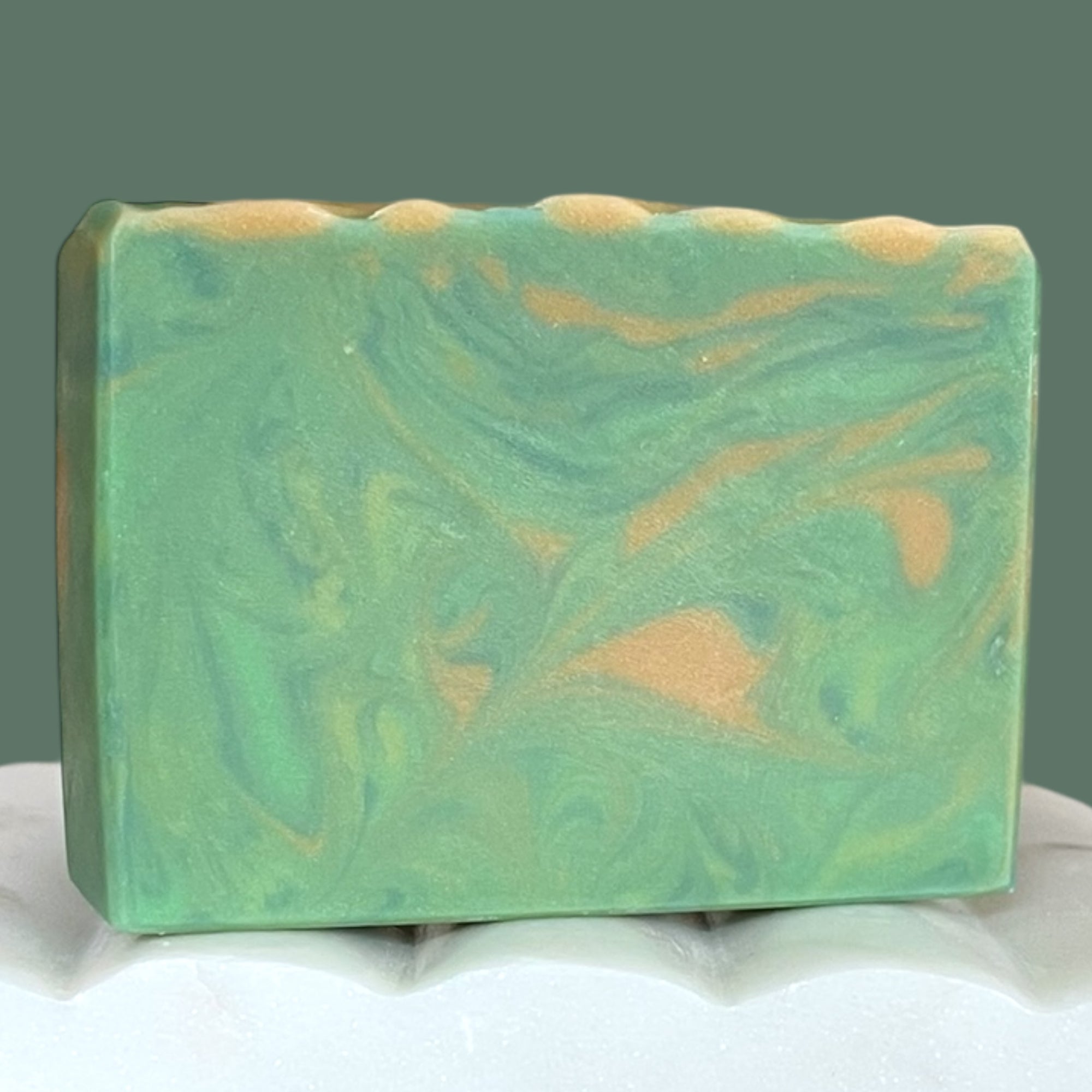 Green and gold marbled soap bar on a white surface with a green background