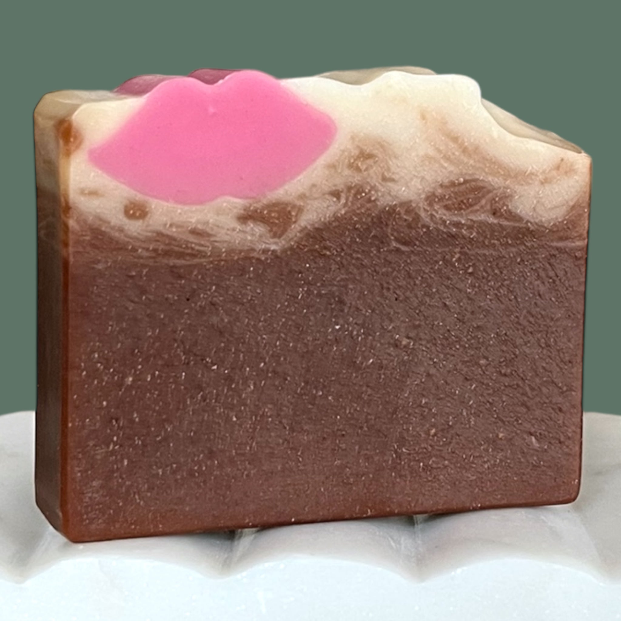 Brown bar of soap with white top and pink lips embed on a white surface