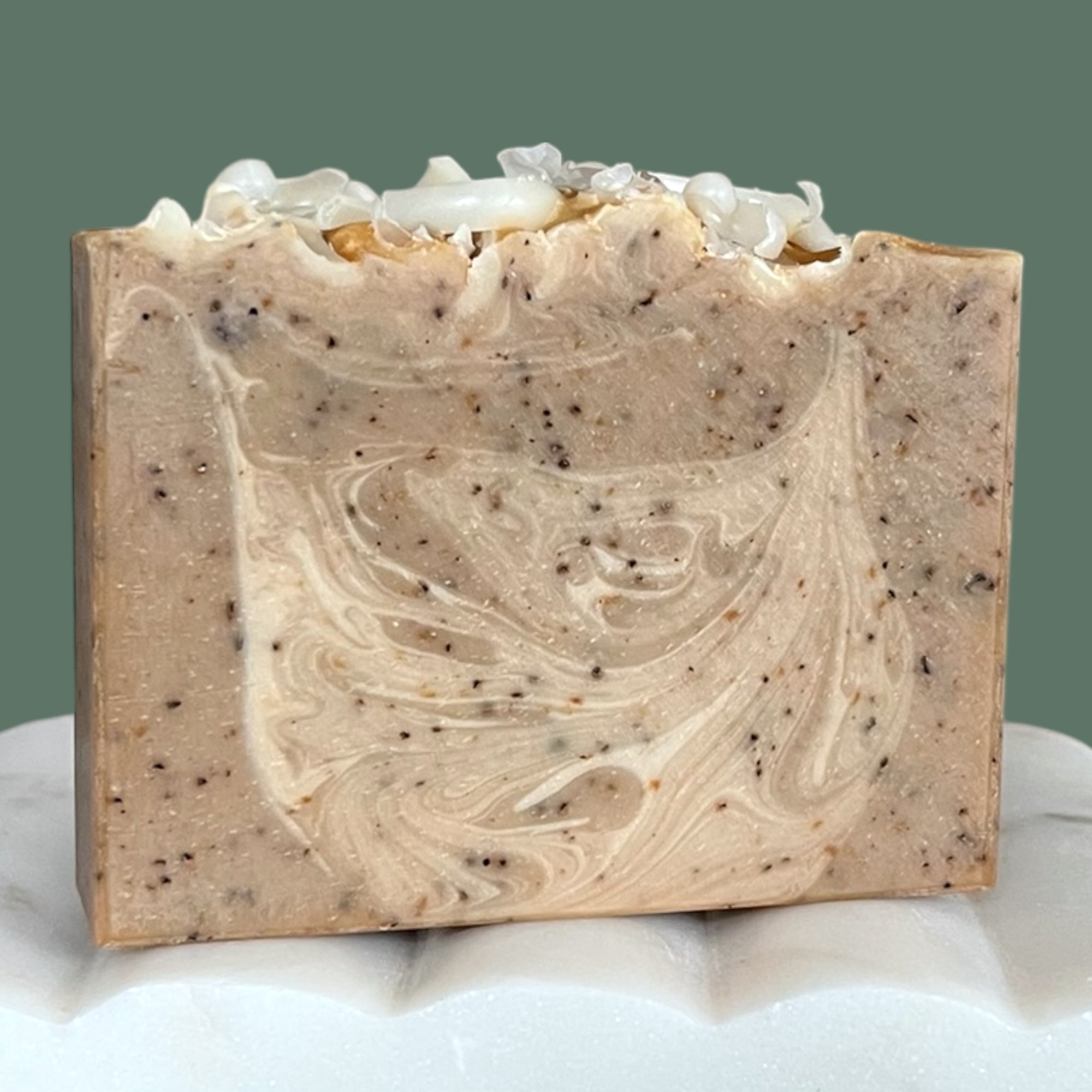 Bar of soap with coffee grounds and a marbled design with shredded white soap top on a white background
