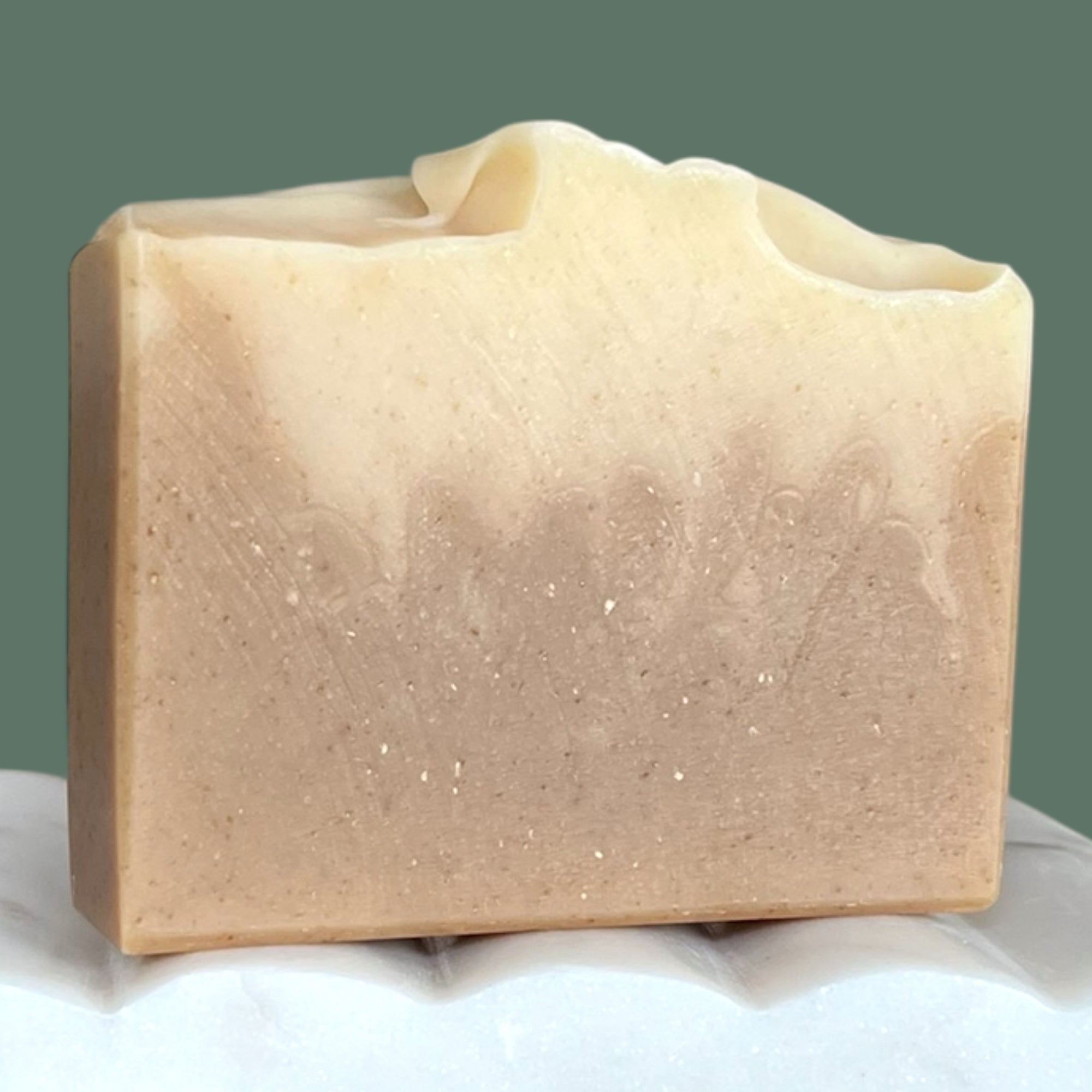 Brown and white gradient colored bar of soap on a white surface with a green background