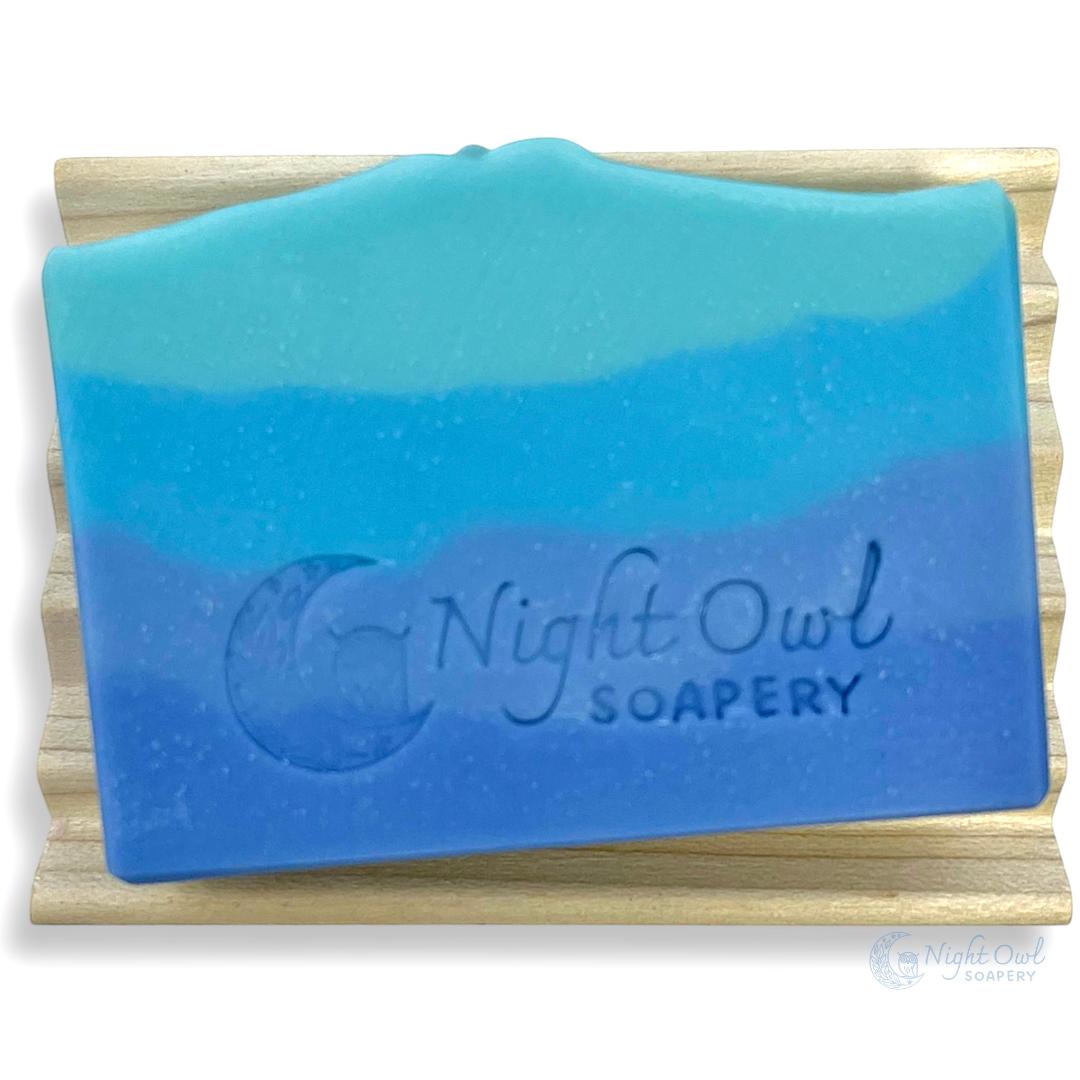 Blue and teal layered soap on a wooden stand with 'Night Owl Soapery' branding.