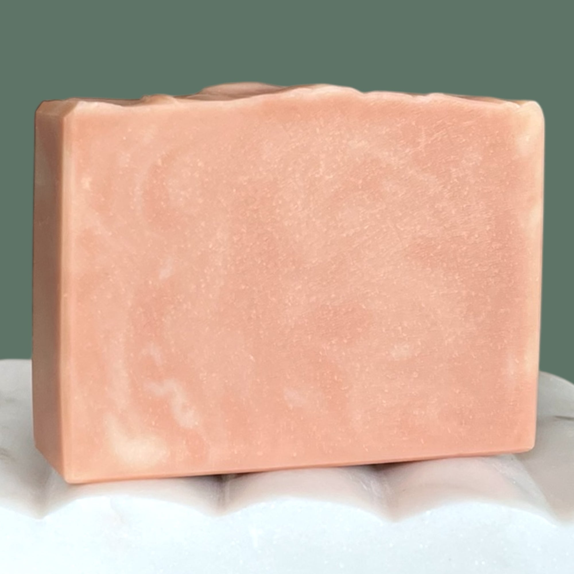 Pink and white swirled soap bar on a white surface with a green background