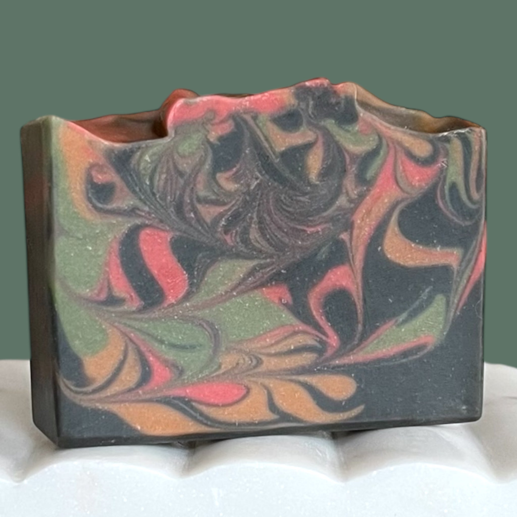 Black marbled soap bar with green, copper and red colors on a white surface.