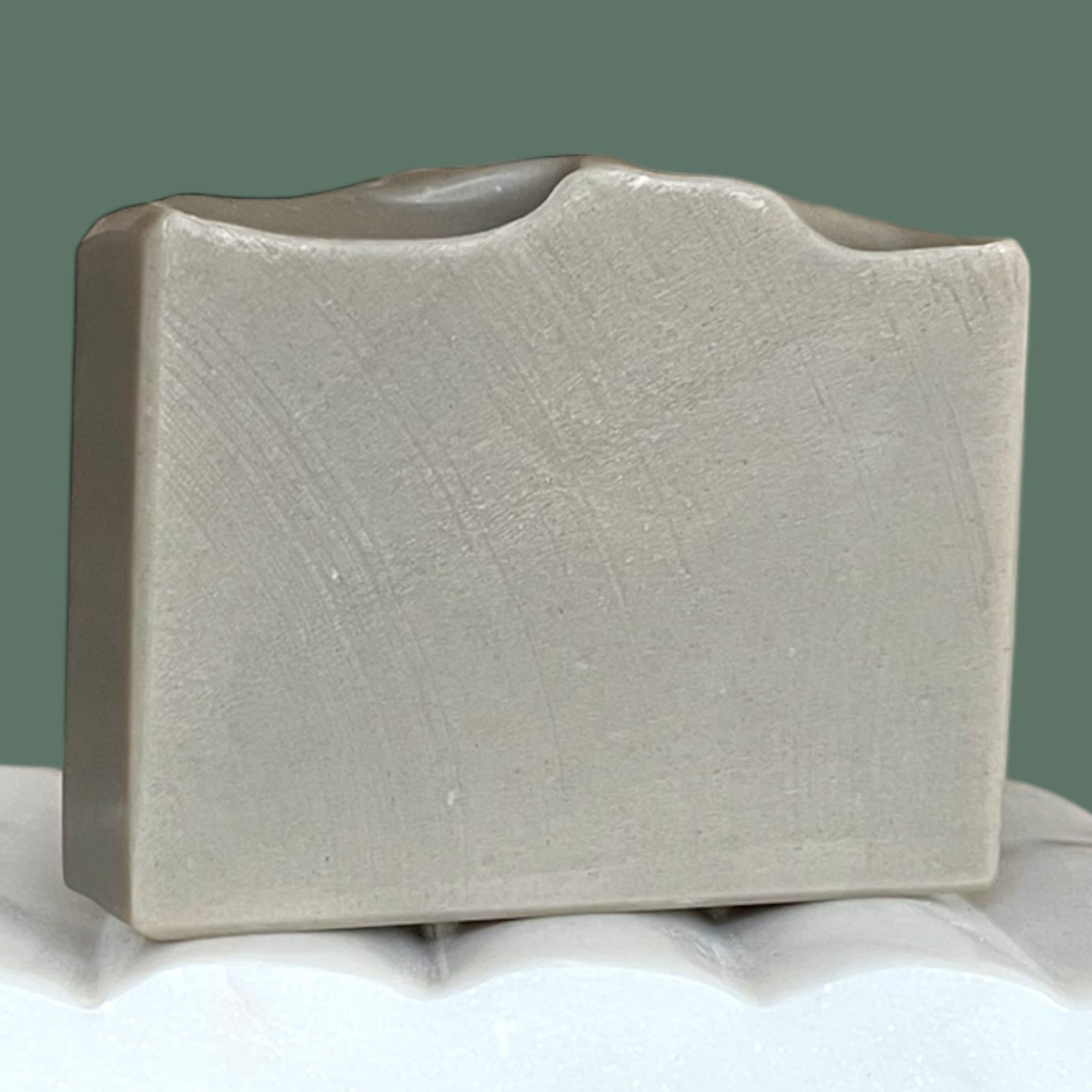 Grey soap bar on a white surface with a green background