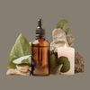 Brown glass bottle with black cap, green leaves, rocks, and a lit candle on a gray background