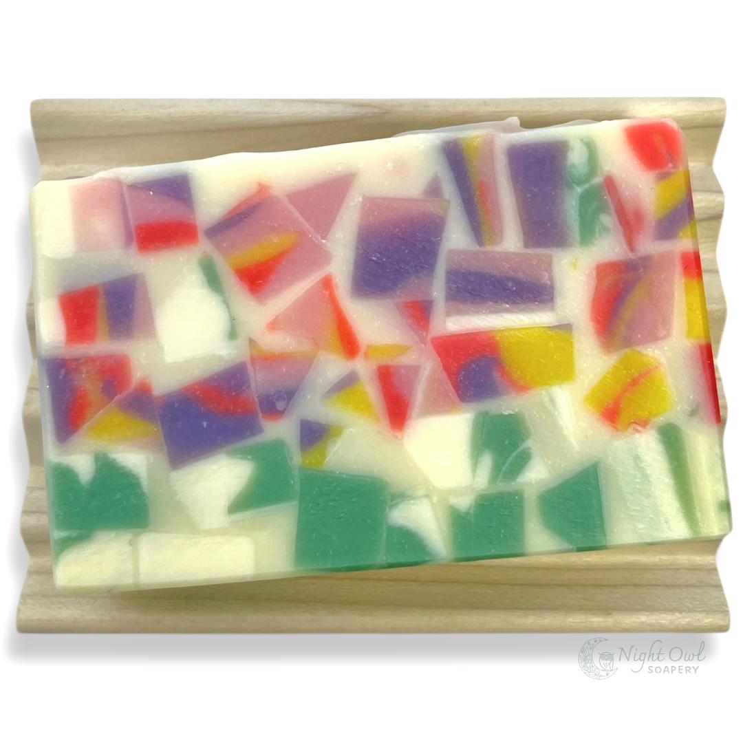 Colorful mosaic soap bar on a wooden soap dish with a white background
