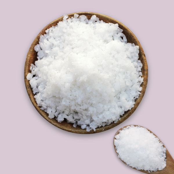 Wooden bowl and spoon filled with sodium hydroxide flakes on a pink background