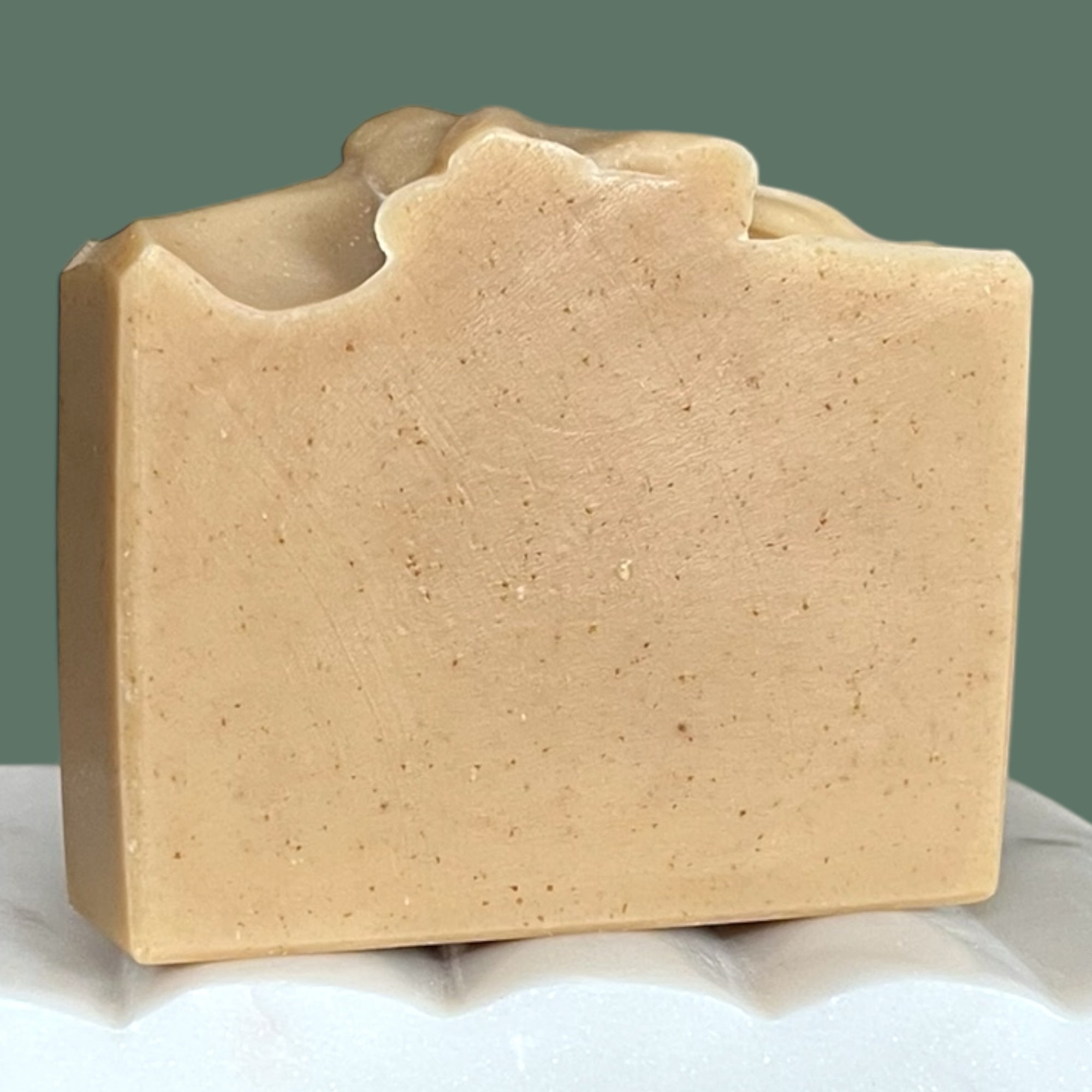 Beige bar of soap on a white surface with a green background