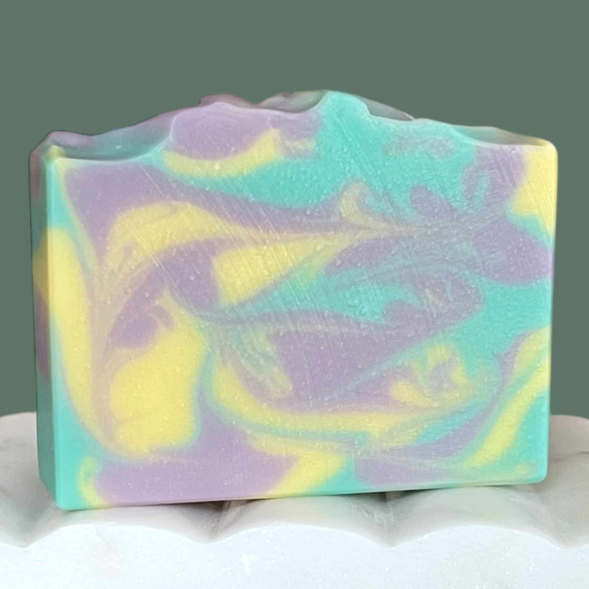 Teal, yellow and purple soap bar with pastel swirls on a white surface