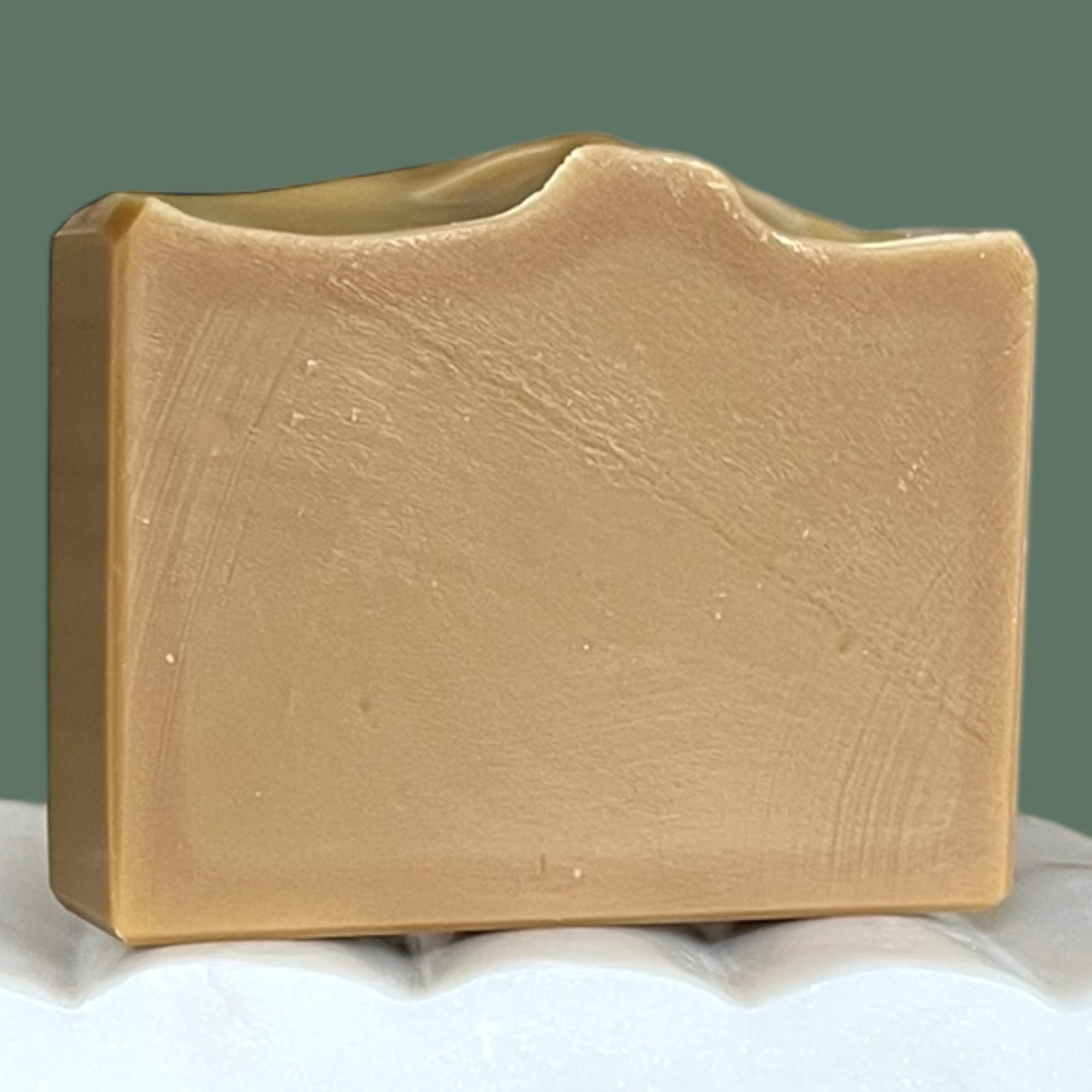 Olive green soap bar on a white surface with a green background