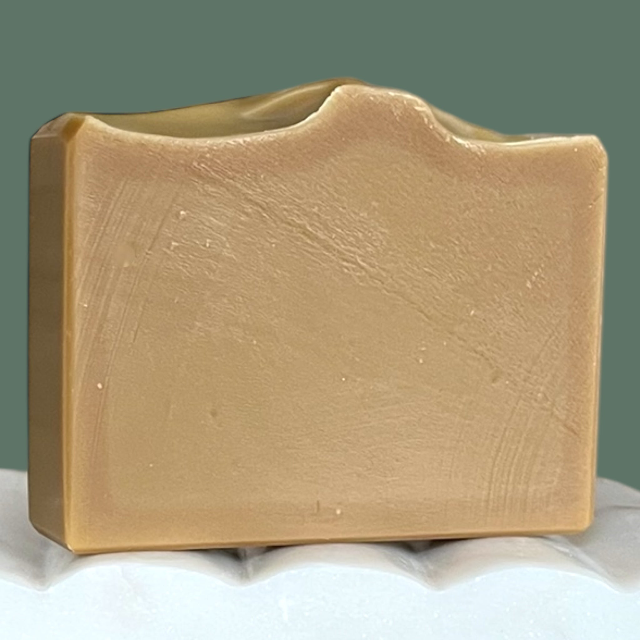 Olive green soap bar on a white surface with a green background