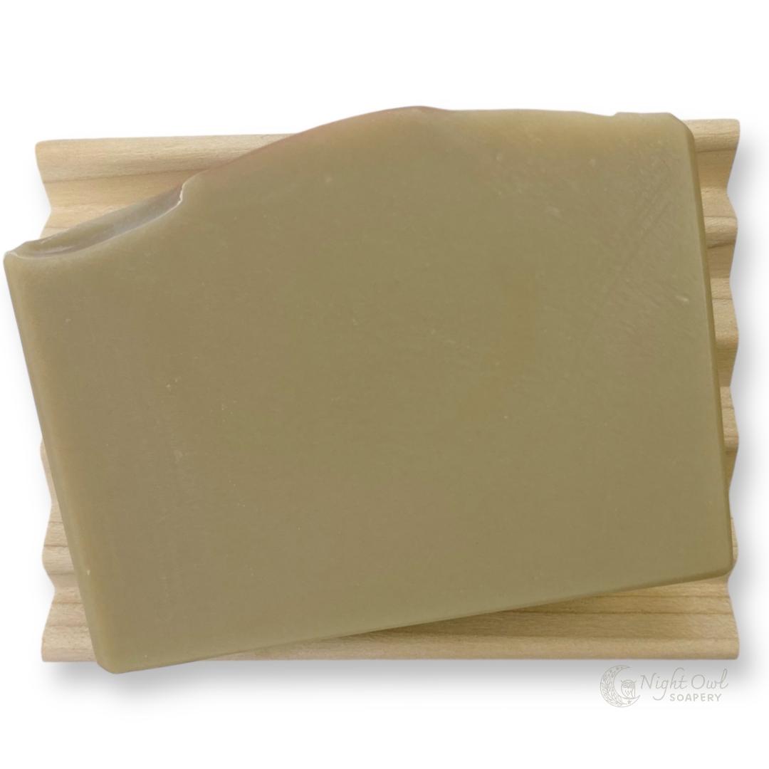 Block of olive green colored soap on a wooden soap dish with a white background
