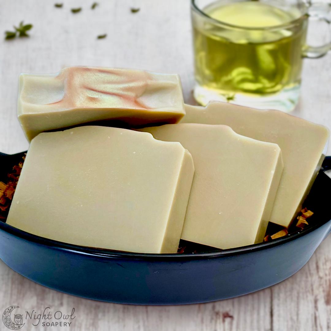 Three bars of soap in a black dish with a glass of green tea in the background.