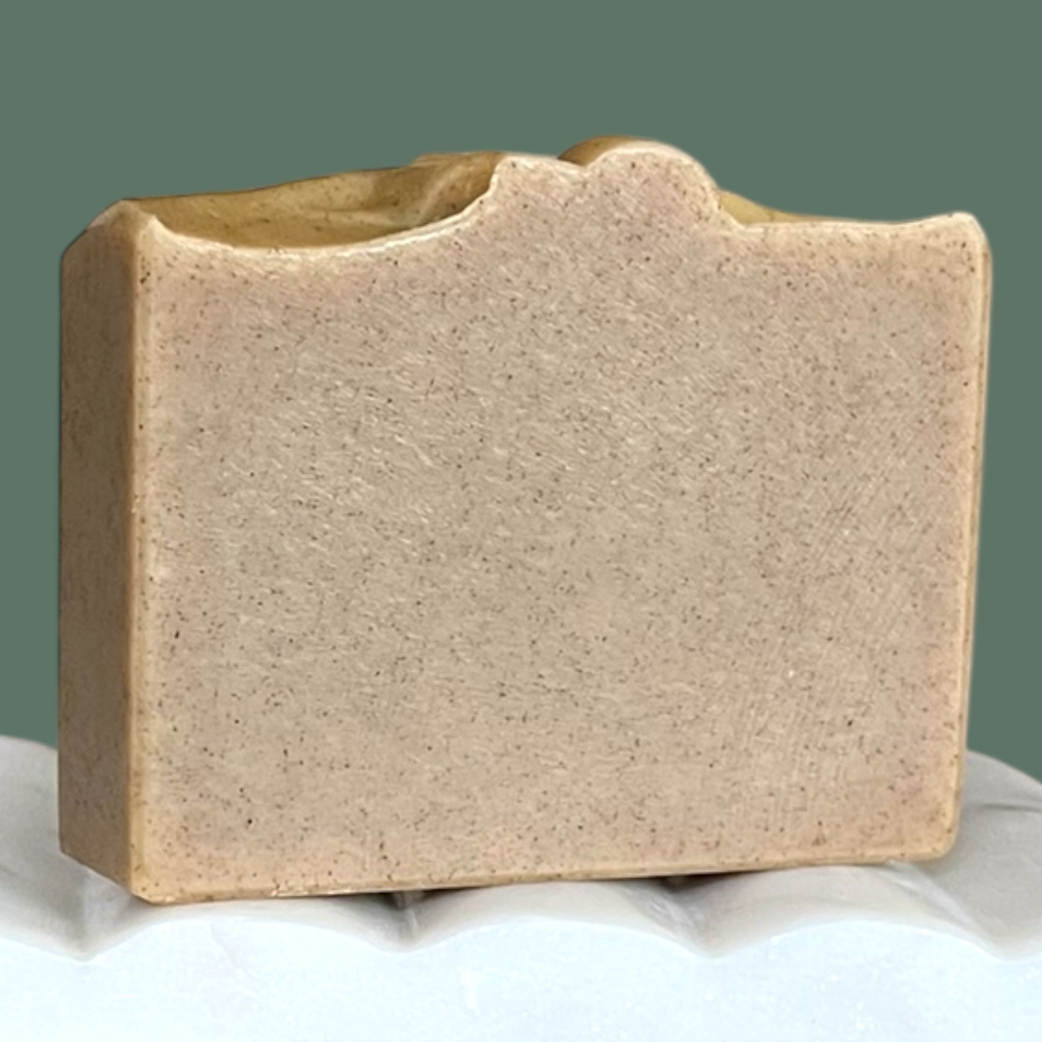 Olive green bar of soap on a white surface with a green background