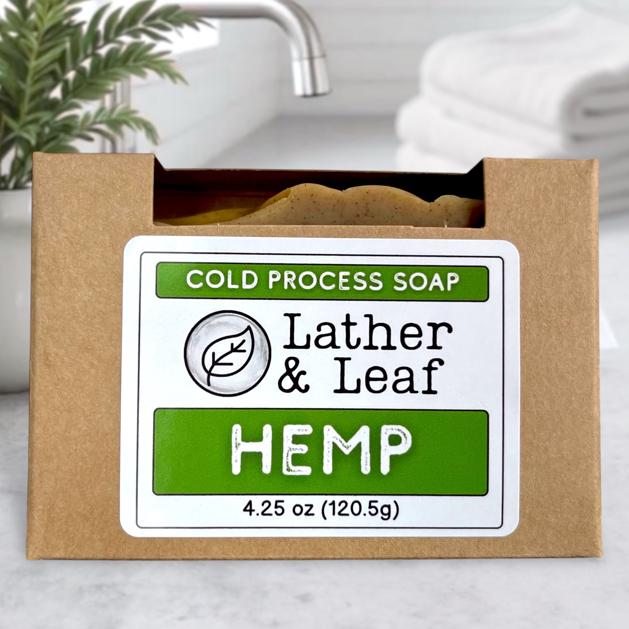 Cold process soap bar in a cardboard box with 'Lather & Leaf' branding on a bathroom counter.