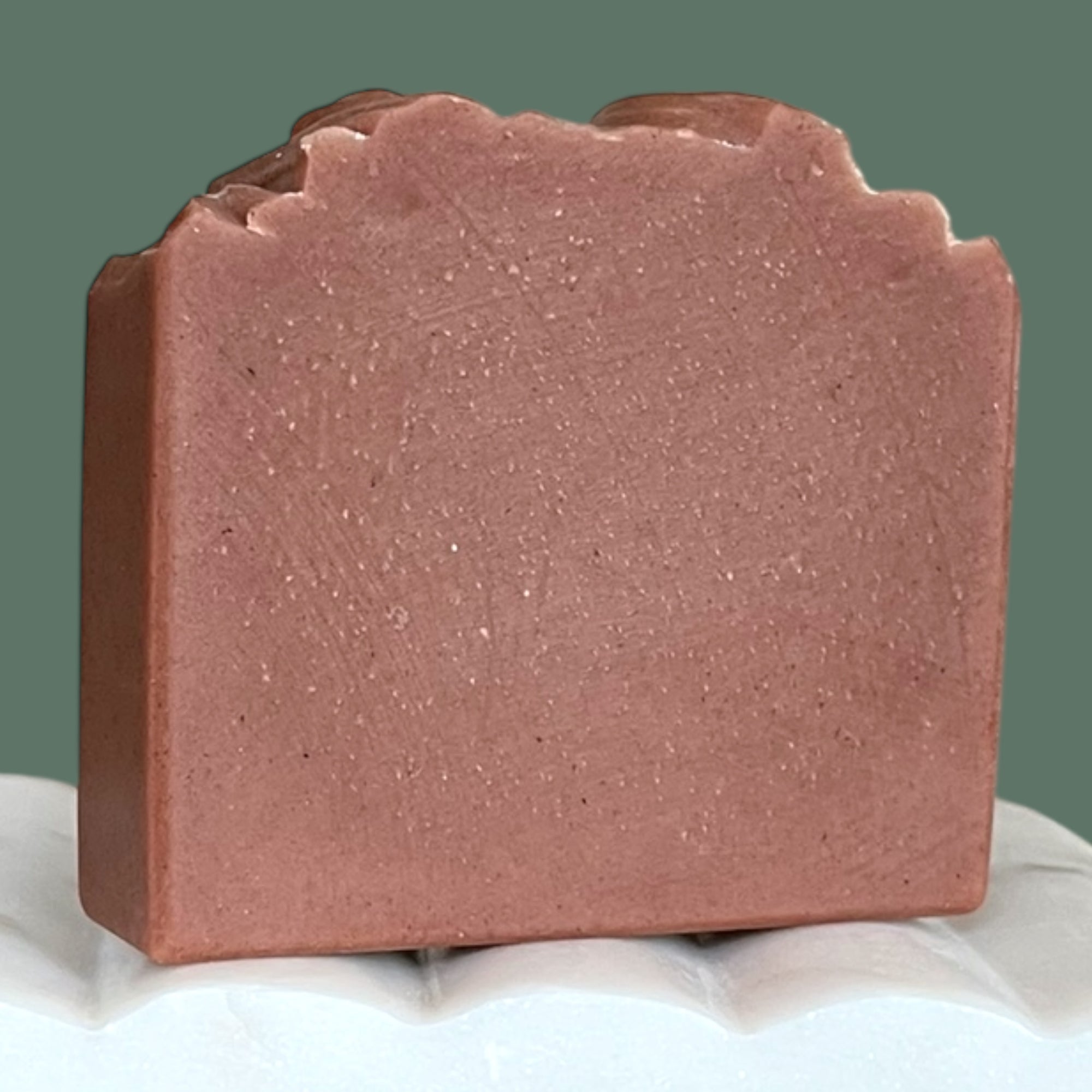 Maroon soap bar on a white surface with a green background