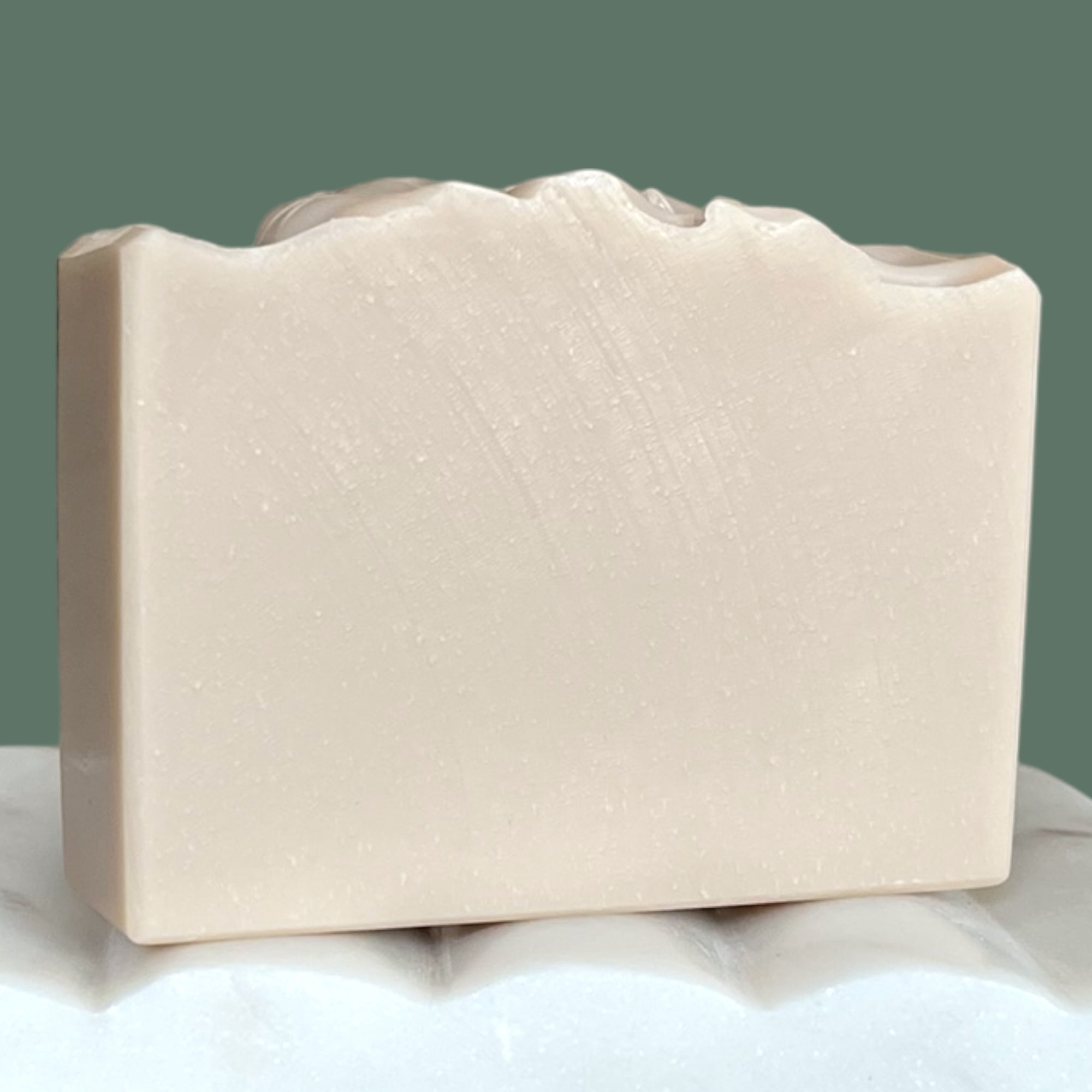 Light purple bar of soap on a white surface with a green background