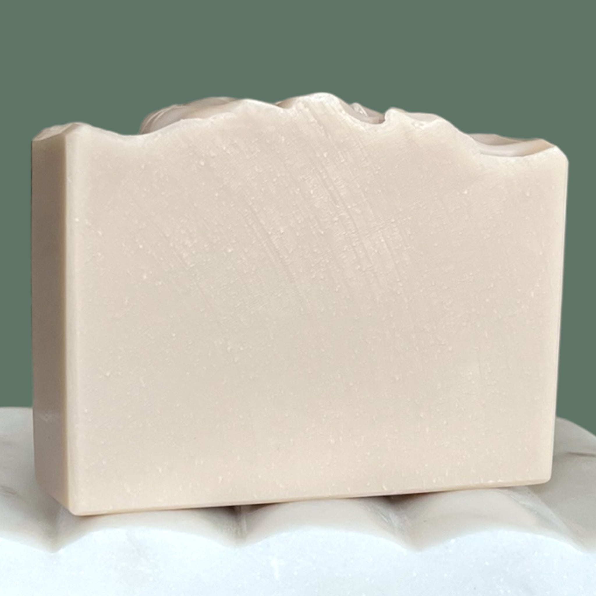 Light purple bar of soap on a white surface with a green background