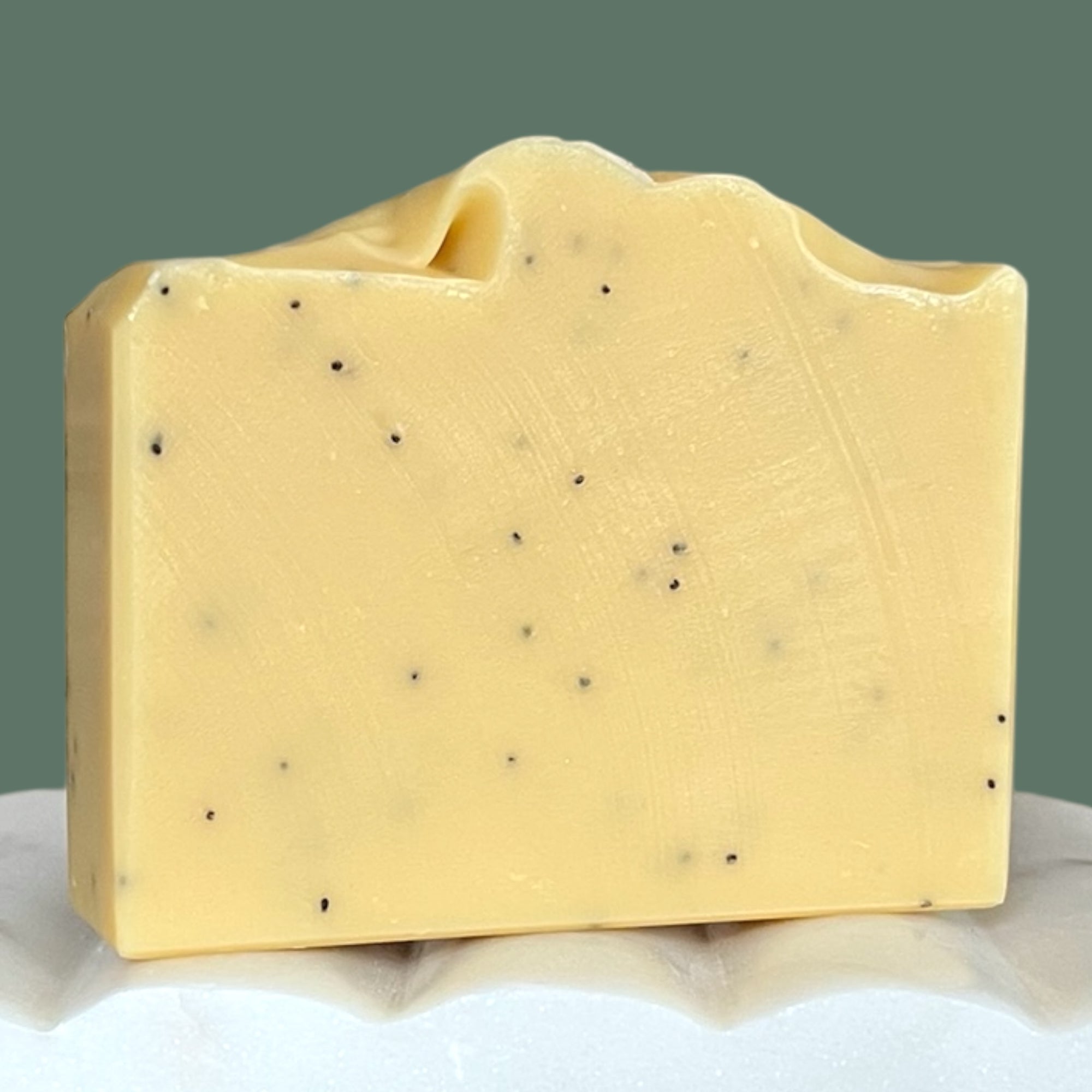 Yellow soap bar with poppy seed specks on a white and green background
