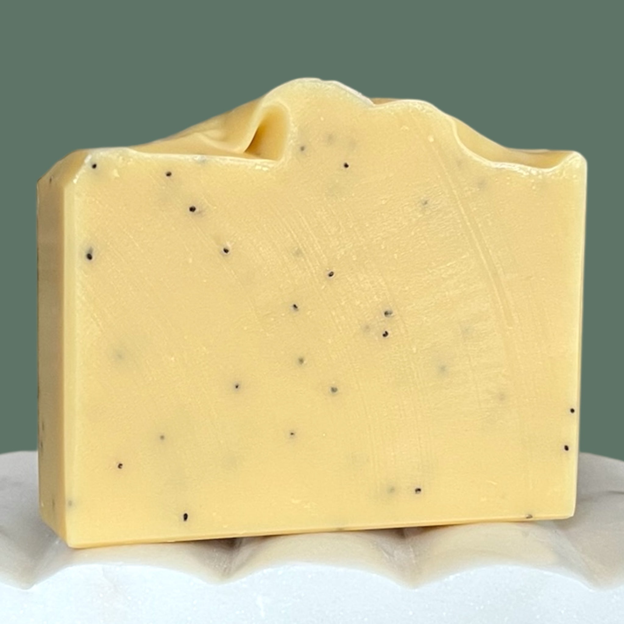 Yellow soap bar with poppy seed specks on a white and green background