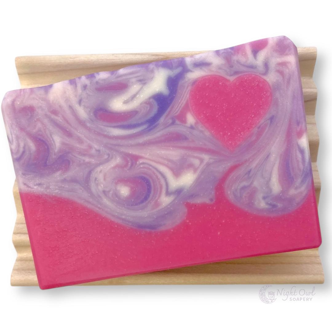 Marbled purple, white and pink soap bar with a pink heart on a wooden soap dish