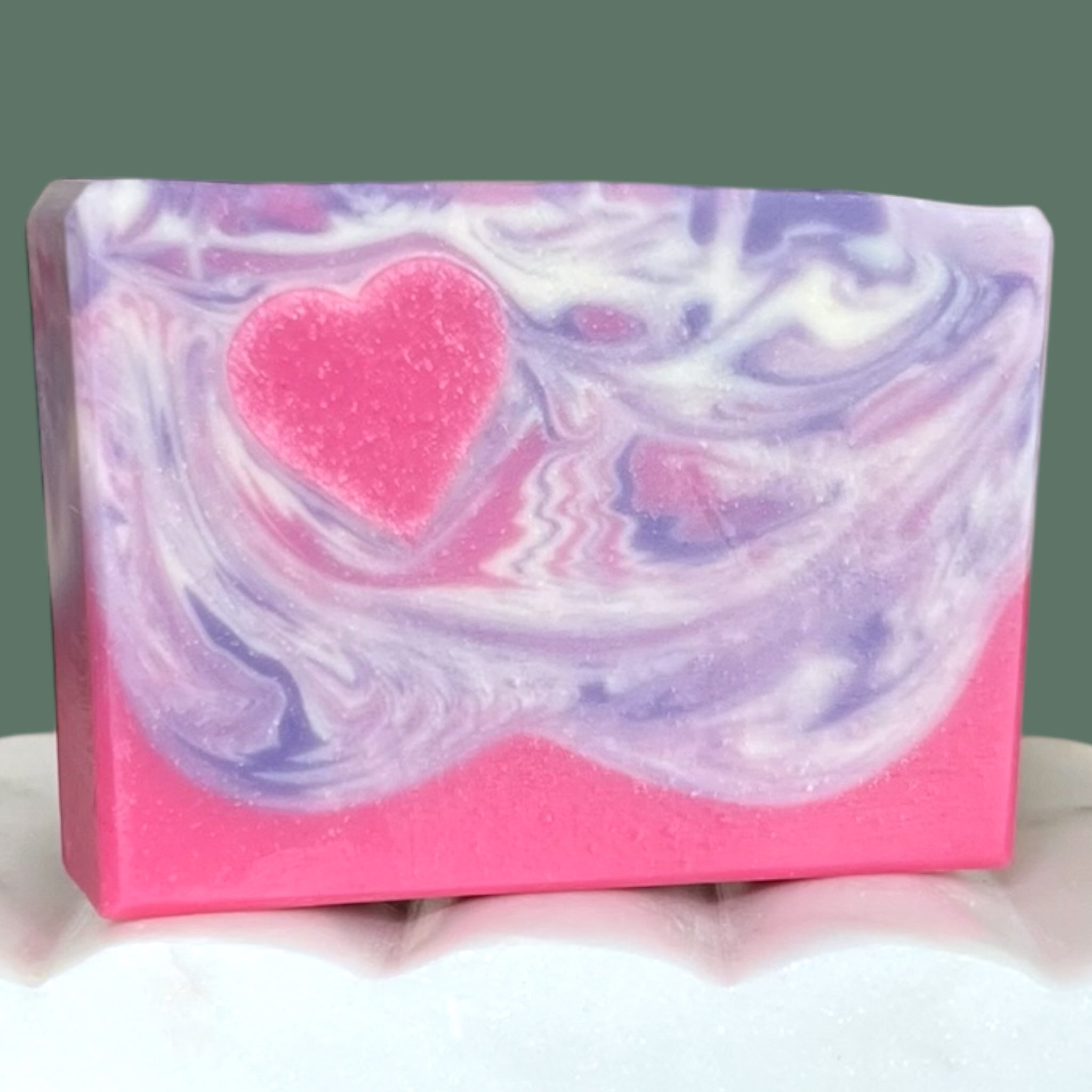 Bar of soap with pink heart and pink, white and purple swirls on a white surface