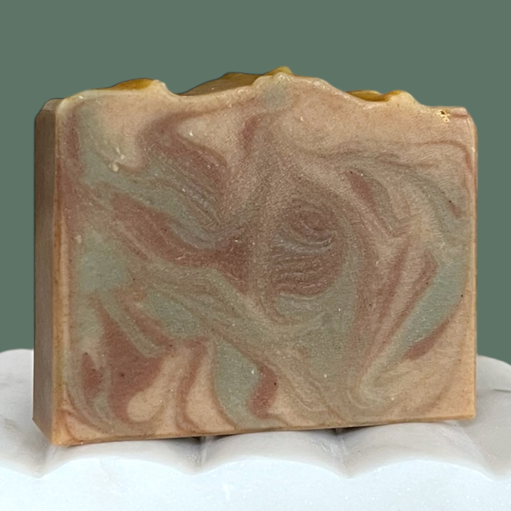 Green, brown and beige swirled soap bar on a white surface with a green background