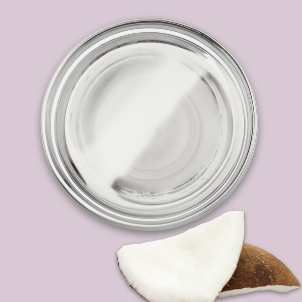 Glass container with coconut oil and a half-coconut on a light purple background