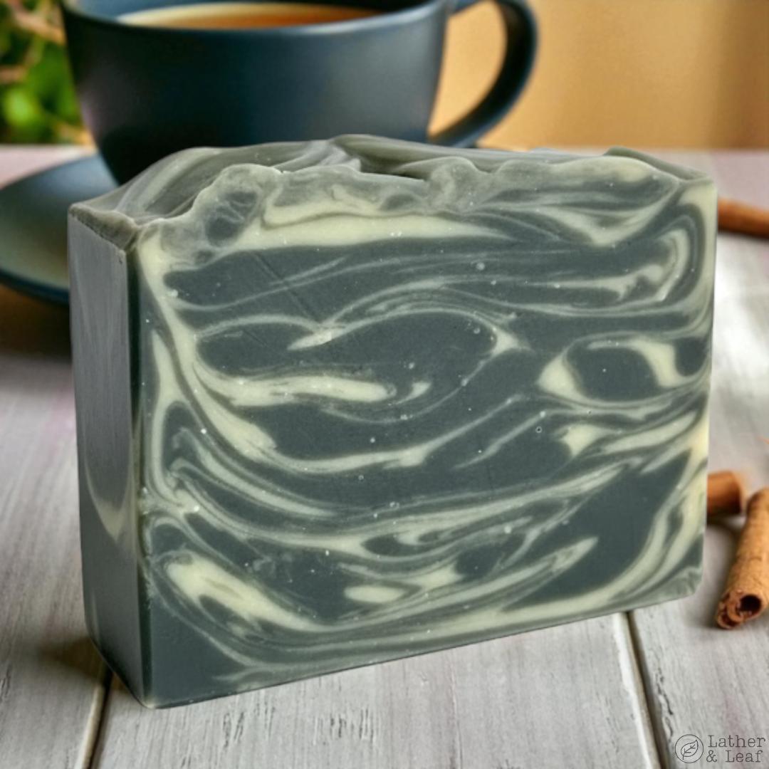 Black and white swirled soap bar on a wooden surface with a blurred tea mug and cinnamon sticks in the background.