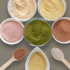 Assorted powders in small containers with wooden spoons on a neutral background