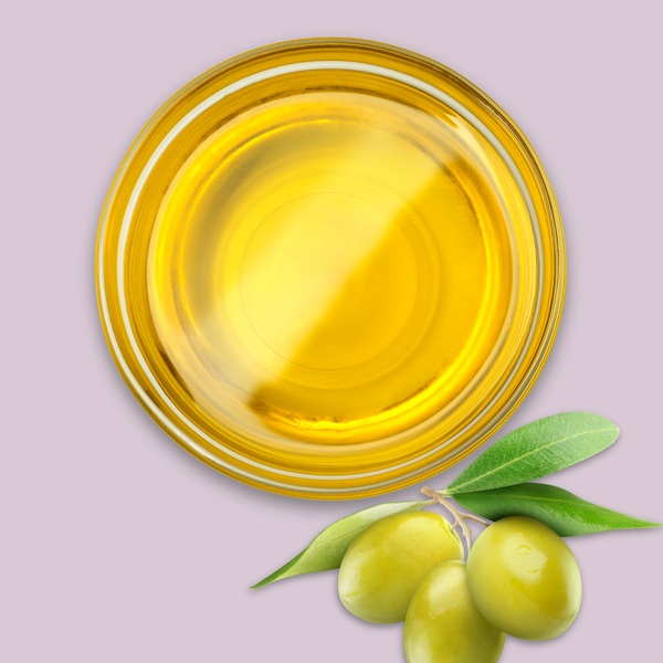 Glass bowl of olive oil with green olives on a light purple background