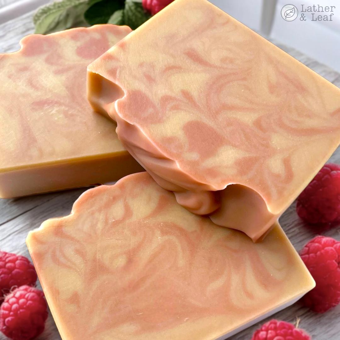 red-pink and beige swirled soap bars on a wooden surface surrounded by raspberries.