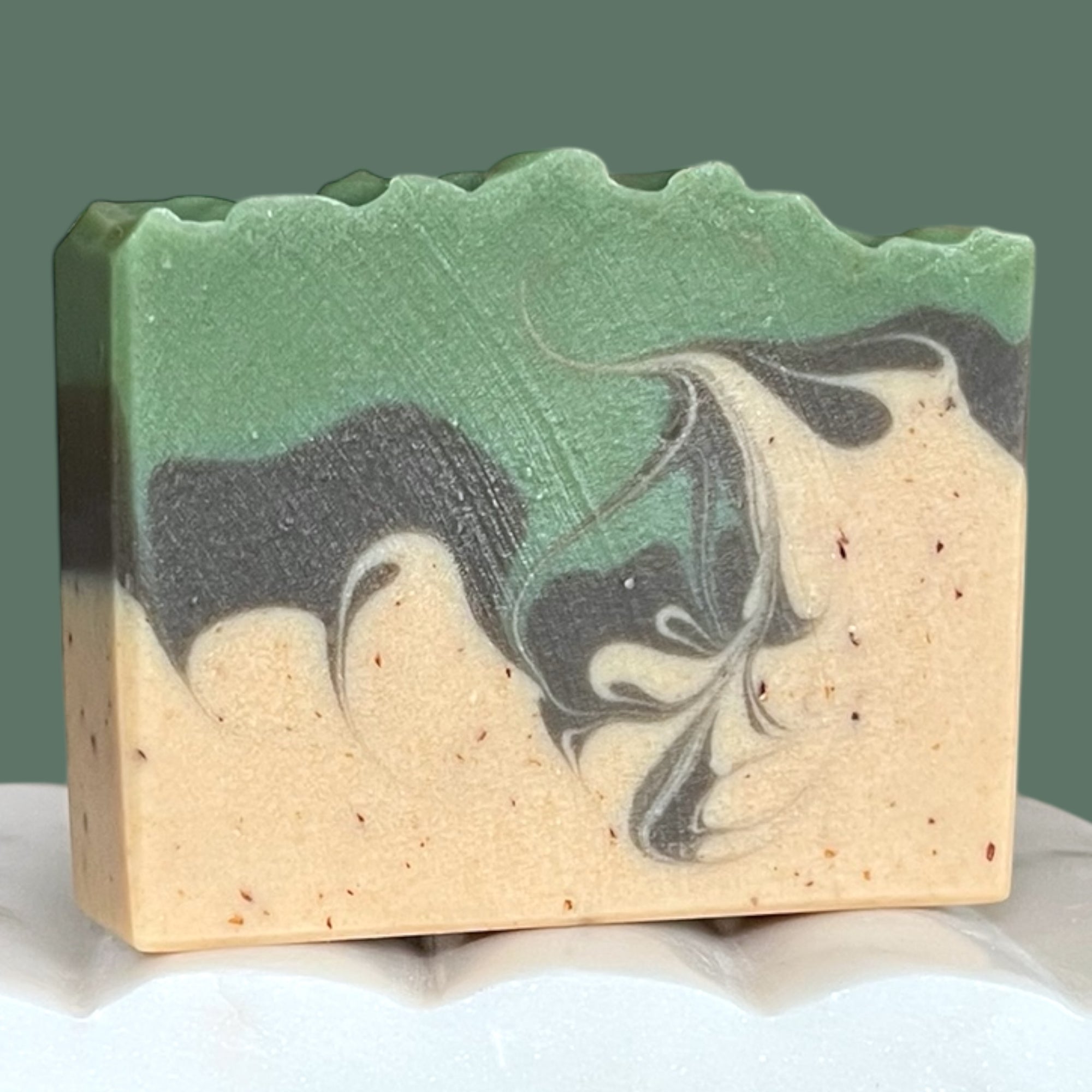 Bar of soap with green, brown, and beige swirls on a white surface