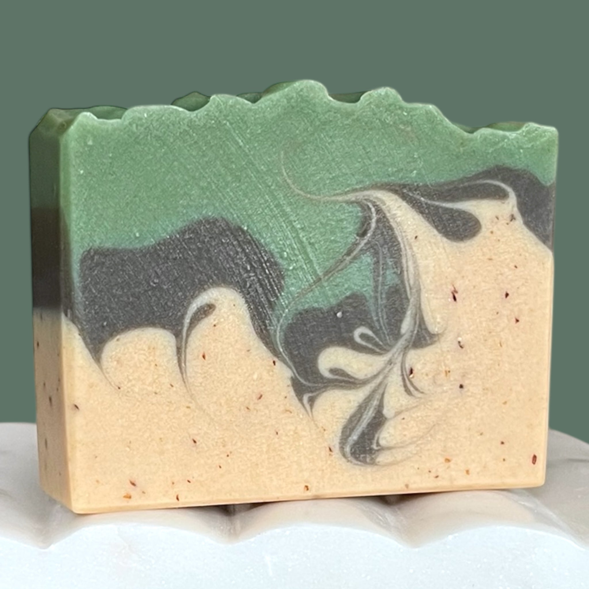 Bar of soap with green, brown, and beige swirls on a white surface