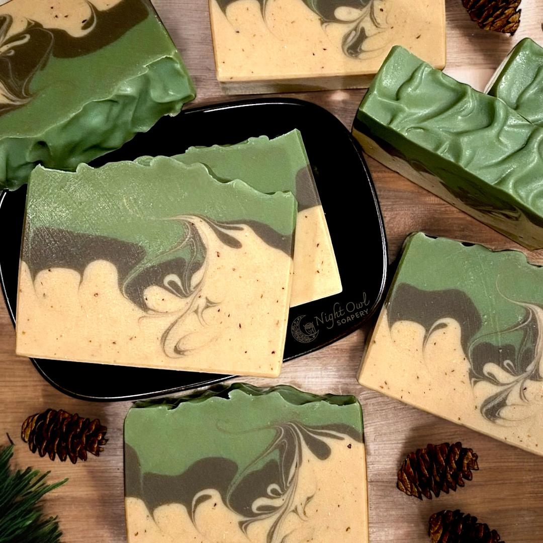 Green, brown and beige marbled soap bars on a wooden surface with pine cones.