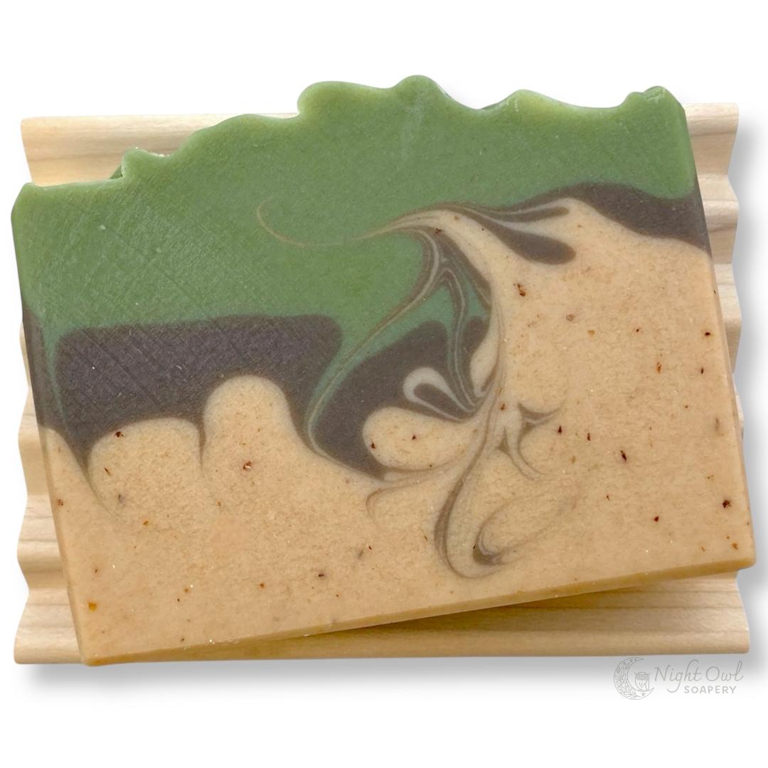 Handmade soap bar with green, brown, and tan swirled design on a white background