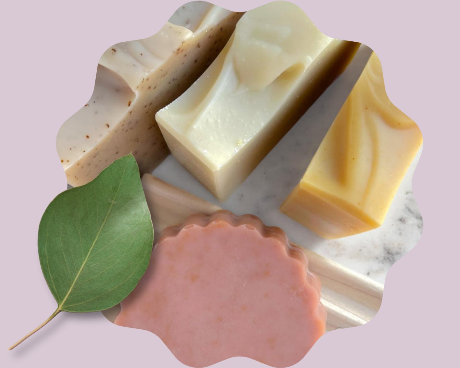 Four soap bars of different colors on a marble surface with a green leaf.