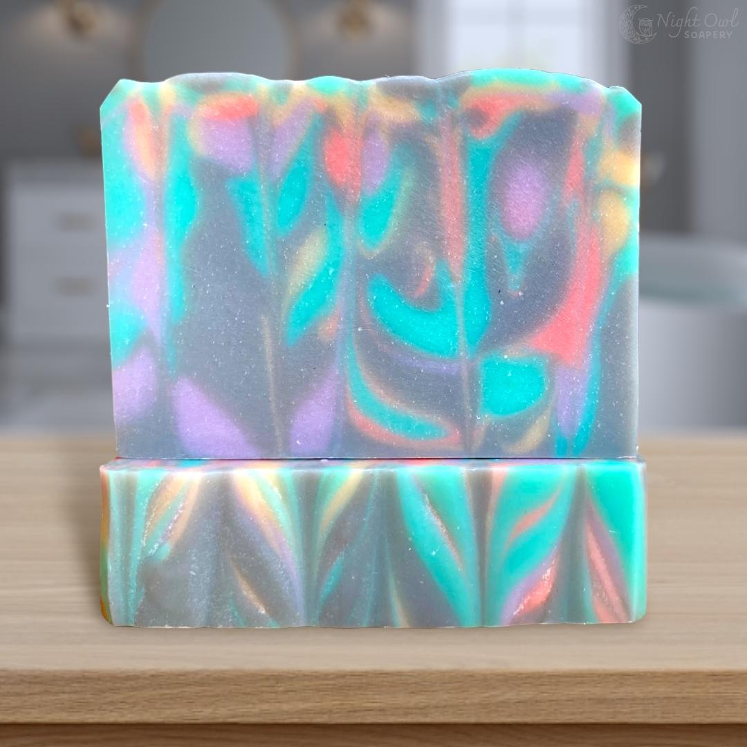 Two colorful soap bars with a colorful abstract flower pattern on a wooden surface.